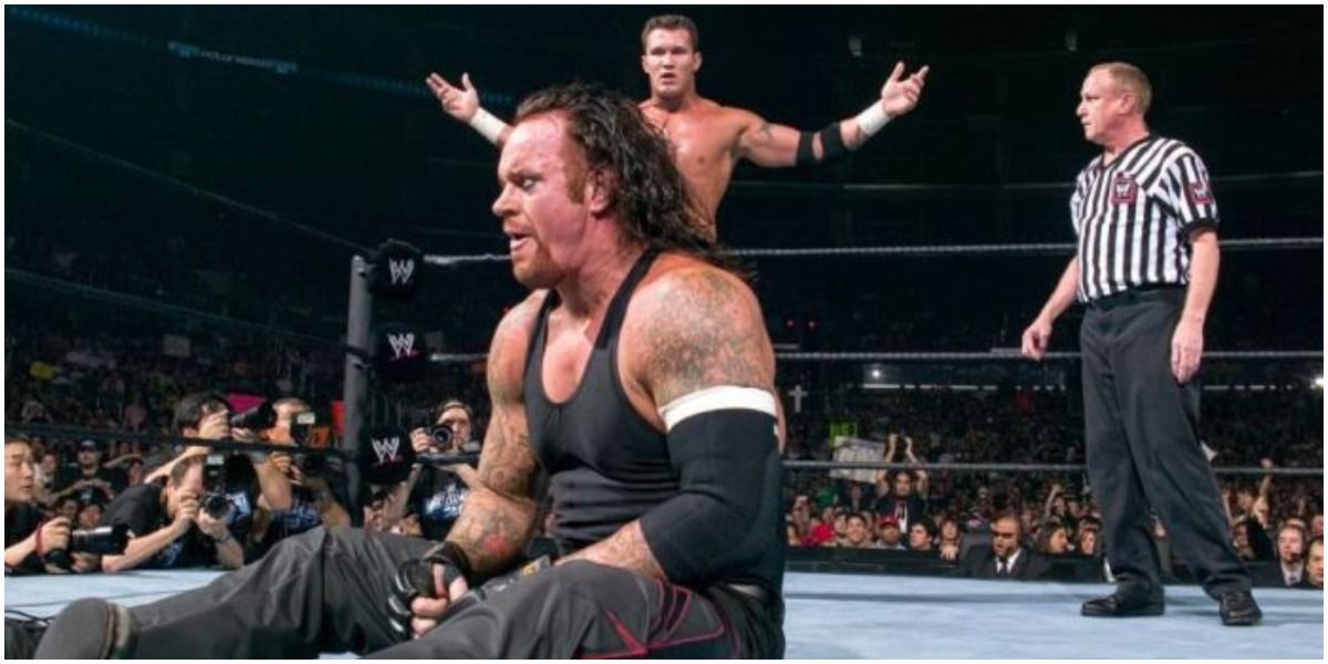 WWE Undertaker Sitting Up In Front Of A Posing Randy Orton