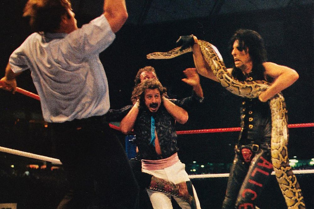WrestleMania 3: Alice Cooper brandishes a snake while Jake Roberts has Jimmy Hart in a full nelson